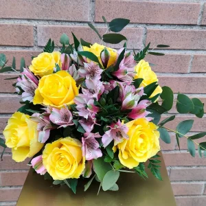 Bouquet allegria di fantasia di rose gialle e alstroemerie rosa su uno sfondo di muro di mattoni.