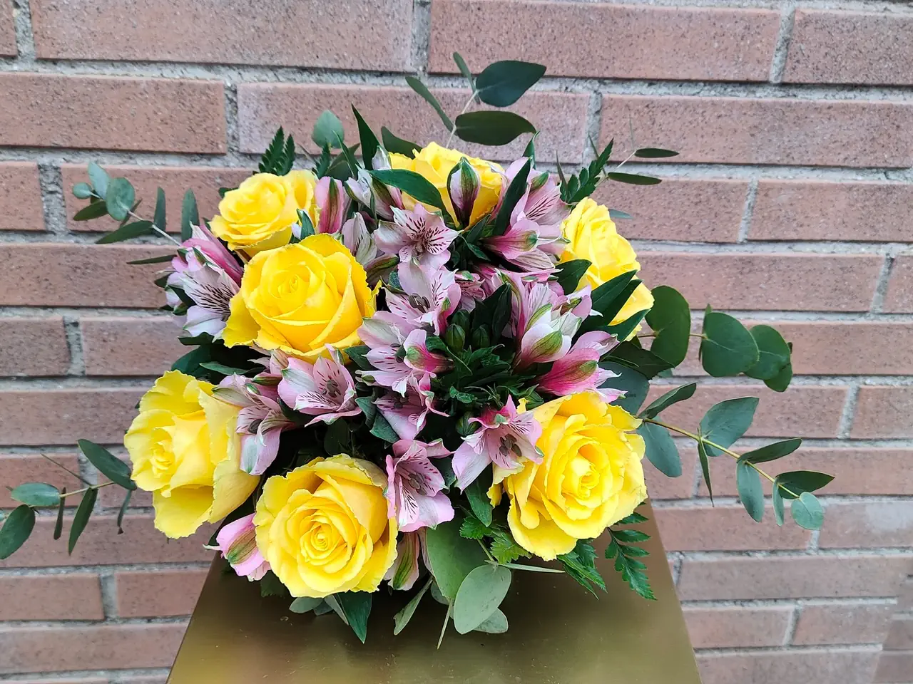 Bouquet allegria di fantasia di rose gialle e alstroemerie rosa su uno sfondo di muro di mattoni.