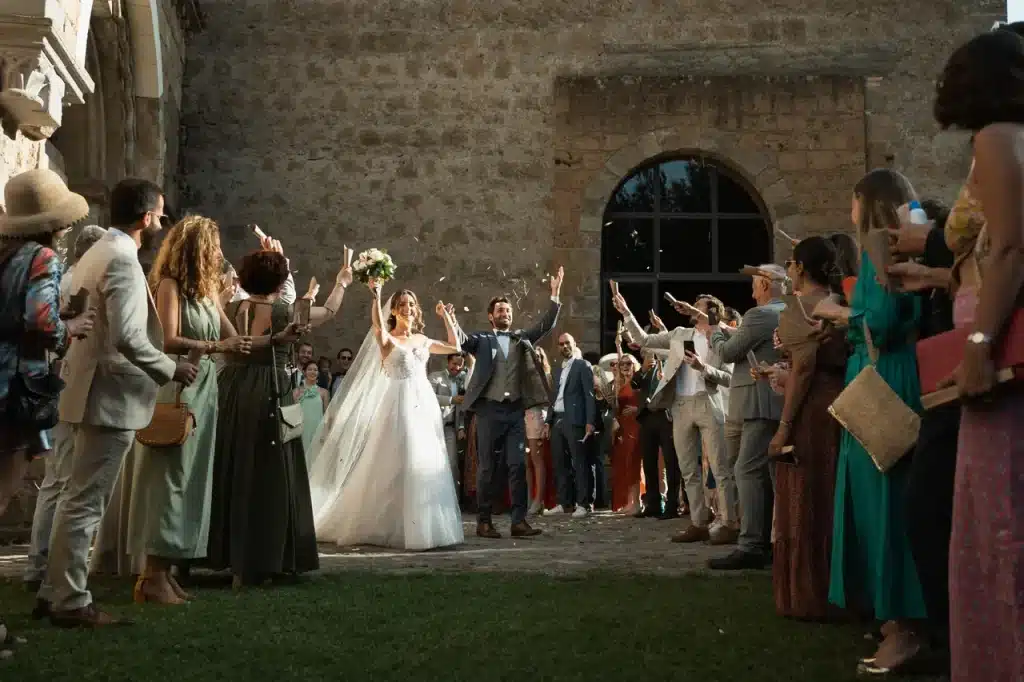 Matrimonio di julie e arnaud: gli sposi festeggiano un matrimonio all'aperto, circondati da ospiti festanti in abiti festosi, vicino a un edificio in pietra.